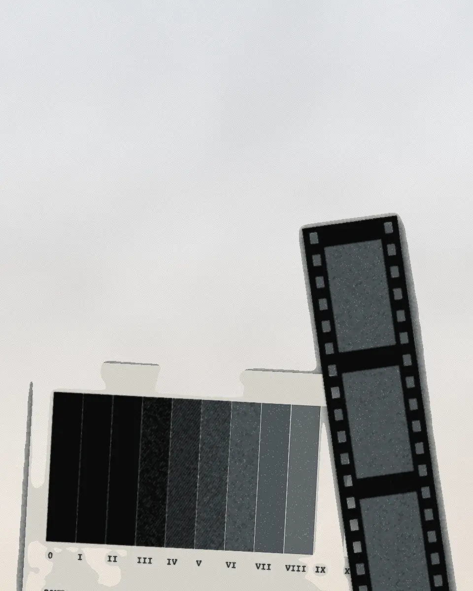 A darkroom step wedge of eleven grey steps numbered 0 to X, exposed onto photographic paper, with a strip of negative lying across its lighter end. The print is in black and a slate ink.