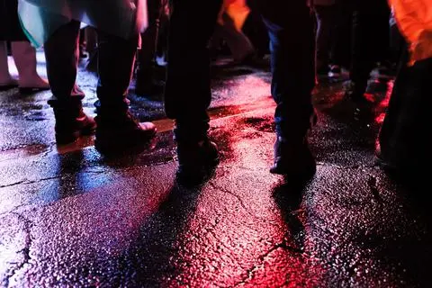Fiestas de Quito, 2025. Boots on wet asphalt in red and blue light.