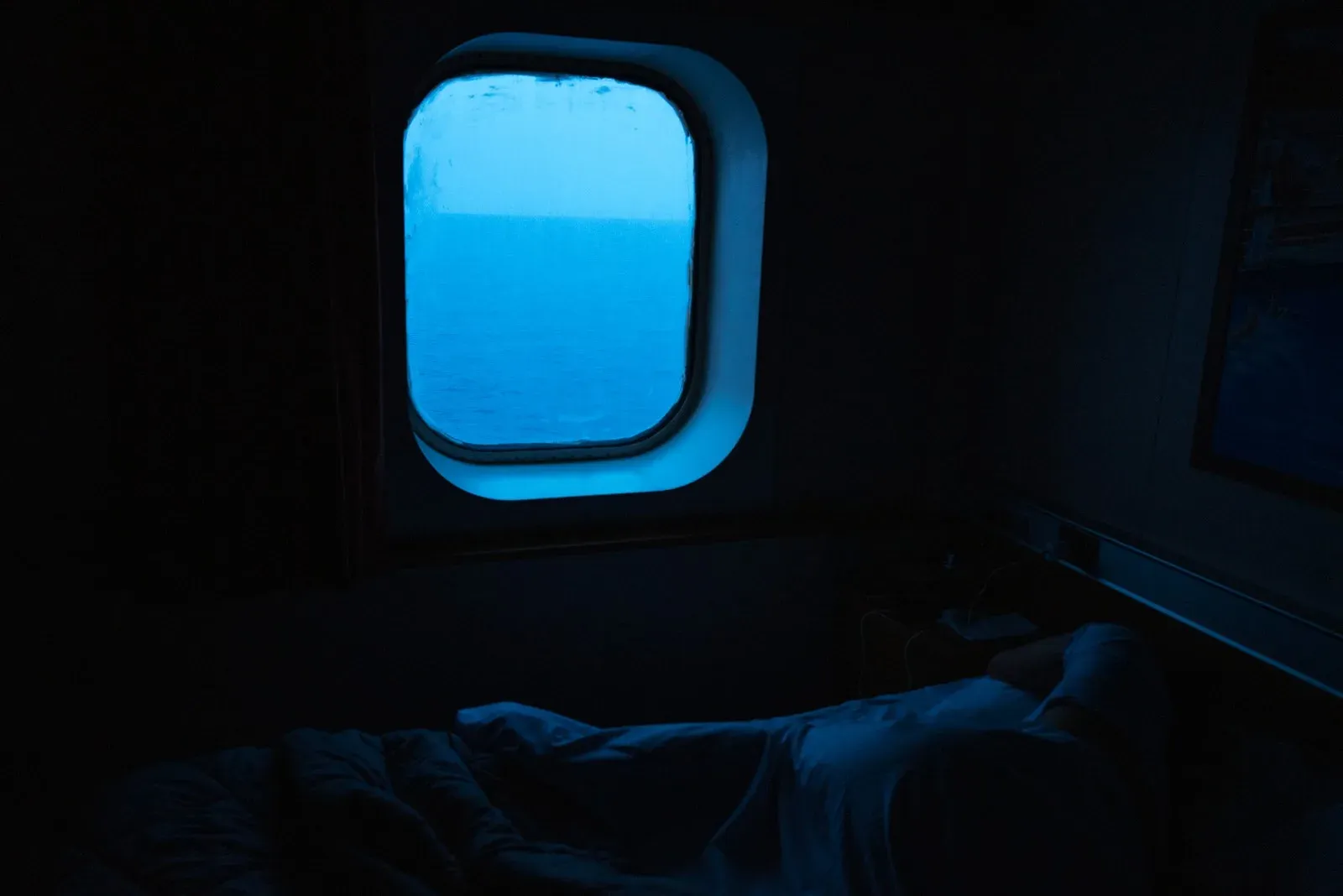 A blue porthole glowing in a dark ferry cabin